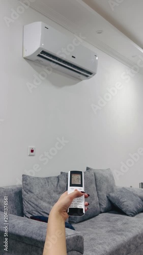 Adjusting air conditioner temperature, 9:16 vertical footage, using AC remote control, cooling room, summer climate control, home comfort, thermostat setting, air conditioning system
