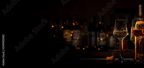 Cuadro en lienzo Glasses of white and rose wine on bar counter with blurred bottles and bokeh lights in background