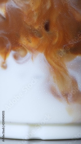 4K close-up of rich espresso swirling and mixing into fresh white milk in a glass, Abstract iced coffee latte texture beverage background, food styling concept.