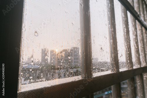 Rainy City Skyline View Through Wired Window with Sunset Glow and Urban Buildings in Background