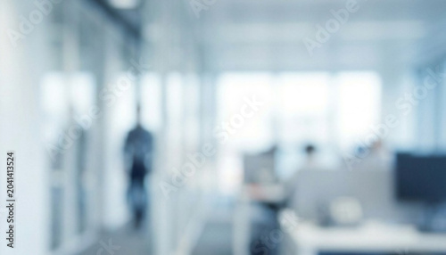 A blurred view of a modern office interior, showcasing workstations and large windows that allow natural light to fill the space.