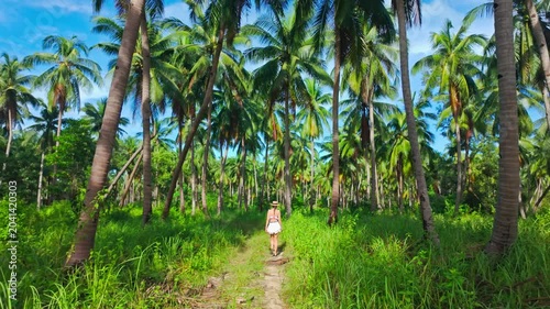 Young woman in white outfit strolls beneath lush coconut trees in paradise