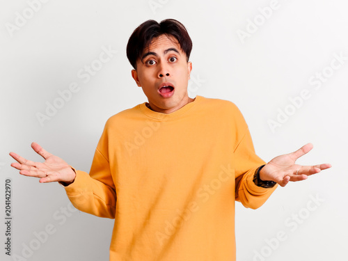 Obraz na plátně A surprised young Asian man in a yellow sweatshirt reacts with a wide-eyed jaw-dropping shocked expression while gesturing with open palms