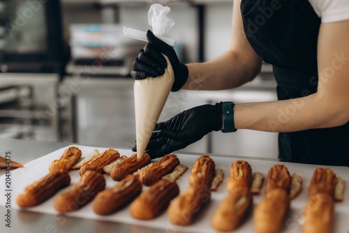Pastry chef filling eclairs with cream using piping bag