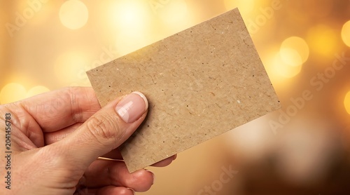 Hand Holding Blank Kraft Paper Card with Bokeh Lights Background.