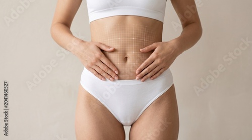 Woman's toned abdomen with markings for cosmetic surgery procedure, she is wearing white underwear and holds her hands