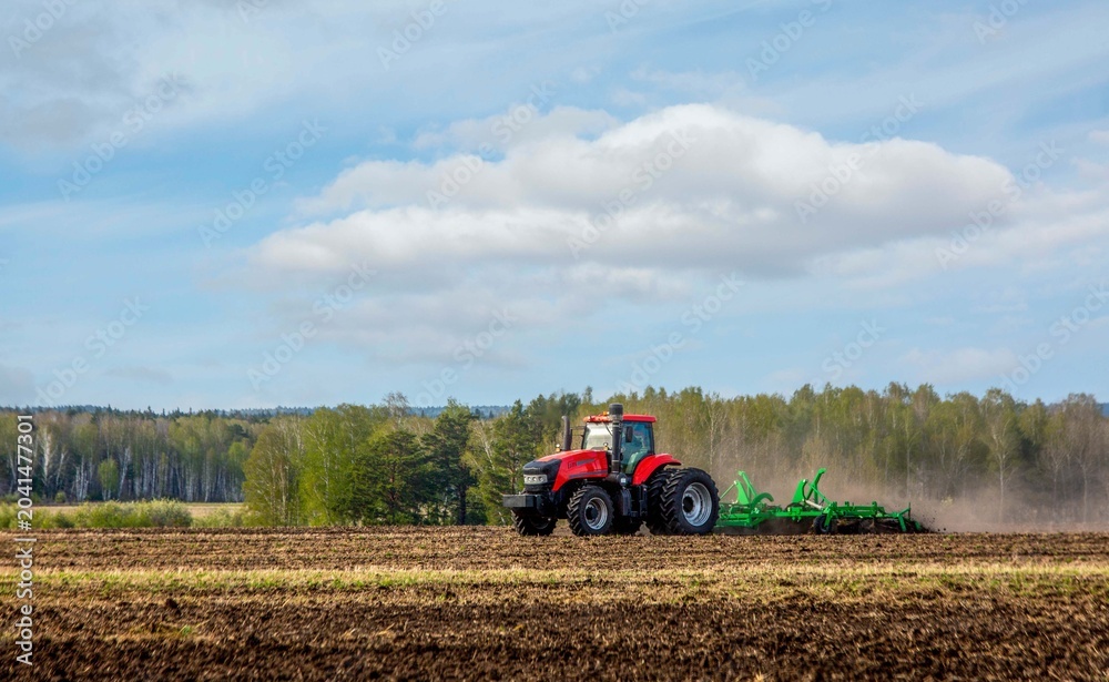 Fototapeta premium A tractor working in a field in spring. Agriculture, farming.