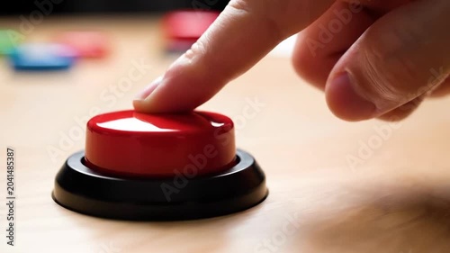 Finger pressing a large red buzzer button on a wooden table. Close-up of hand pushing a start or alert button. Decision and action concept