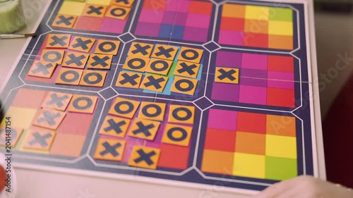 child's hand placing tile with X onto colorful board during game tic tac toe, Fine motor skills practice, detailed shot focusing on move and interaction, puzzle solving, Strategic thinking for kids
