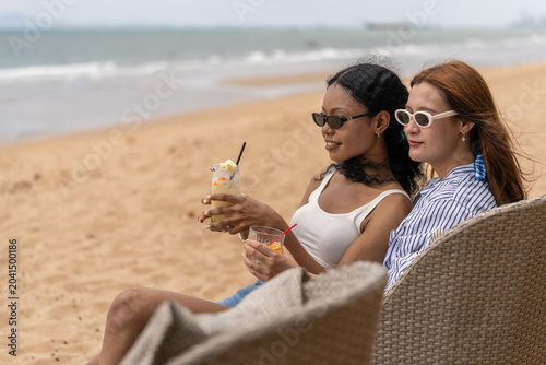 Foto Happy lesbian couple drinking cocktail on the beach during summer vacation, Two