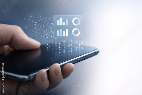 Hand holding smartphone with data analytics charts and particles mobile phone technology