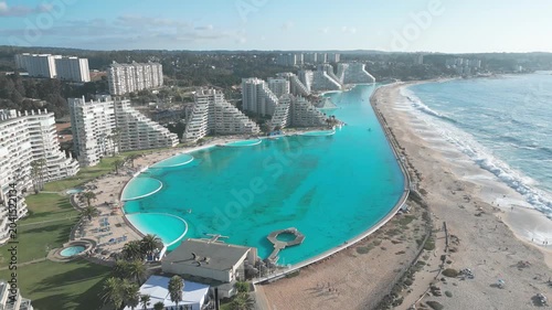 Pull back flight over San Alfonso del Mar revealing the full extent of the worlds largest turquoise pool flanked by resort towers and Pacific Ocean beach. Algarrobo, Chile