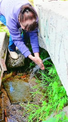 A woman draws water from a natural spring that is located under a concrete slab.