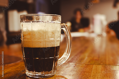 Canvastavla Dark stout beer in a mug with white foam on wooden bar counter, enjoying an alco