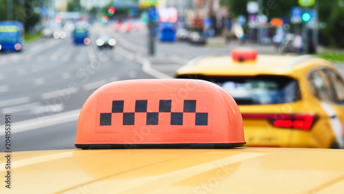 Tableau sur toile Taxi cab roof sign with checkered pattern on a city street, urban traffic moving