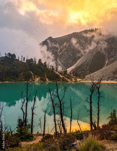 Turquoise Crater Lake Reflecting Dramatic Sunset Sky and Misty Mountains.