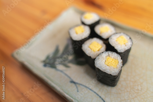 Six pieces of tamago maki sushi on a decorative plate.