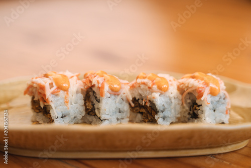 Sushi roll with crab stick shreds, white rice, orange sauce, and garnish on a wooden plate.
