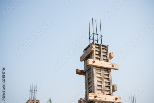 Concrete column formwork with steel reinforcement bars at a construction site under clear sky.