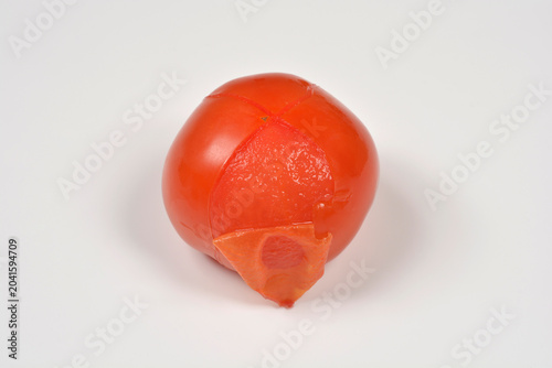 Photos A whole ripe red tomato scored with a cross at the top and partially peeled afte