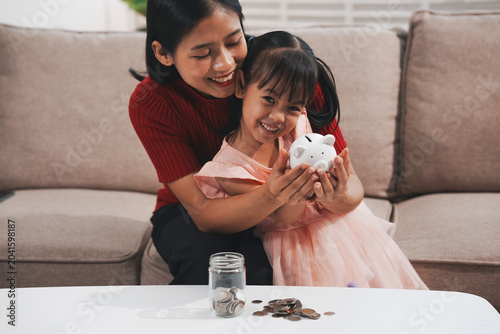 Tableau sur toile A young mother is setting a good example, teaching her little daughter about financial management and saving money