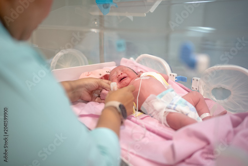 Nurse Caring for Crying Newborn Baby Inside Hospital Incubator