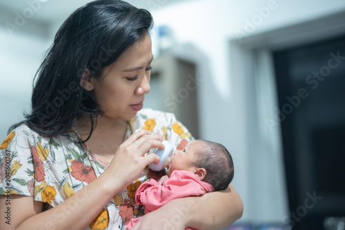 Loving Asian mother bottle-feeding her newborn baby while cradling the infant in her arms at home.