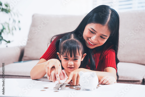 Tableau sur toile A young mother is setting a good example, teaching her little daughter about financial management and saving money