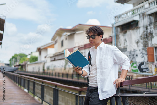Young man traveling, reading book on city street bridge