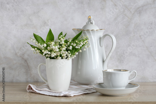 Foto Delicate lily bouquet in white mug with porcelain teapot and cup on neutral gray background, concept of spring tea time and elegant home decor
