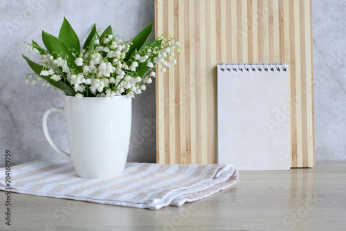 Bild auf Leinwand Blank spiral notepad mockup beside lily of valley bouquet in white mug on neutral background, spring design and space for your text