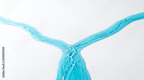 Blue water stream splitting into two paths on a white surface