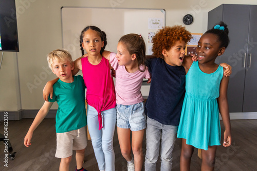 Bild auf Leinwand Five children standing with arms around each other in classroom near whiteboard