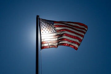American flag waves beside national banner. Bright sunlight passes through American flag. July celebration features patriotic American flag. American flag symbolizes freedom and liberty.