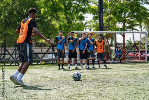 African American soccer player taking free kick shot during football match. Diverse opponents defensive wall standing near goal post waiting for ball outdoor