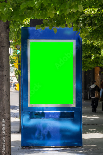 Urban advertising billboard with green screen mockup on city street sidewalk