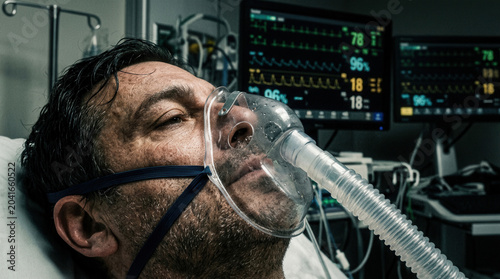 Patient In Intensive Care Unit With Oxygen Mask And Electronic Monitors Displaying Vital Signs