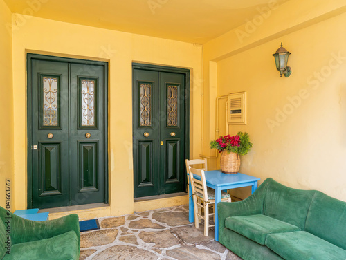 Cozy traditional patio with green doors, blue table, and lush flowers in the historic Plaka neighborhood, Athens.