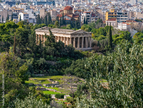 A scenic view of the Temple of Hephaestus in Athens, Greece, with urban city buildings visible in the distance.