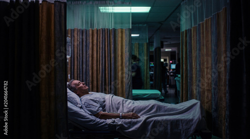 Patient Resting in Bed Inside Hospital Room After Medical Procedure in Low-Light