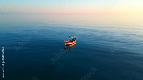 Tranquil fishing boat floating on calm ocean with serene reflection at sunrise or sunset