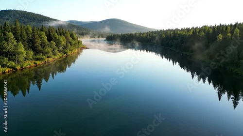 Scenic aerial view of a tranquil lake surrounded by lush green forests on a sunny morning, featuring a solitary boat.