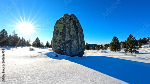 Bright Winter Day with a Large Boulder in a Snow Covered Meadow Under a Clear Blue Sky