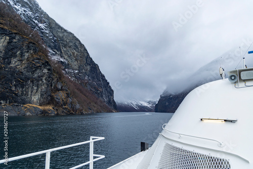 A beautiful winter cruise day on an electric tour ferry with deck details in foreground.. Winter scenery in Geirangerfjord, Sunnmore region, Norway.