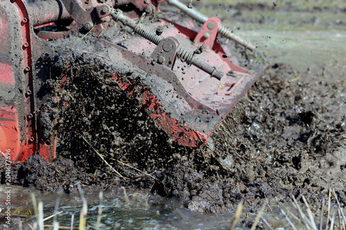 Tractor tilling muddy rice field with splashing water and soil. Agricultural machinery working in wet farmland, ideal for farming, rural life, and cultivation concepts, close-up