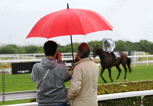 Foto Público y afición en hipódromo con paraguas rojo espectador fotografiando caball