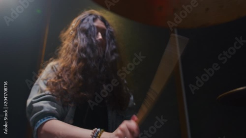 Portrait: female with long curly hair plays the drums. Girl is rehearsing in a studio with drumsticks. Face of a beautiful musician girl, showcasing skill and energy. Underground indie slow motion