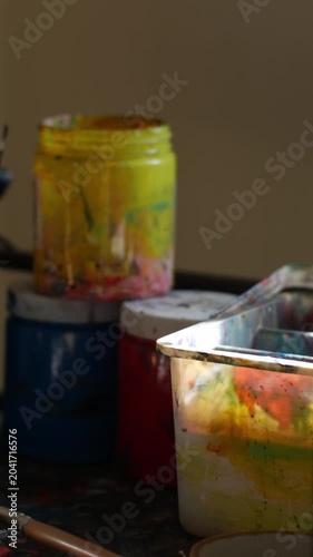 Messy artist studio table with acrylic paint brushes jars tubes and palette showing creative working process in natural light