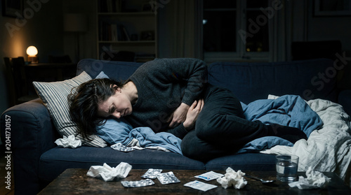 Woman Suffering From Abdominal Pain on Couch in Dimly Lit Room at Night