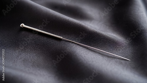  Slender silver acupuncture needle on dark silk fabric. 